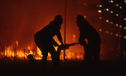 806140 Afbeelding van de silhouetten van twee brandweermannen tijdens het blussen van de in brand staande houten ...